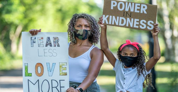 A woman and young girl hold signs encouraging love and kindness.